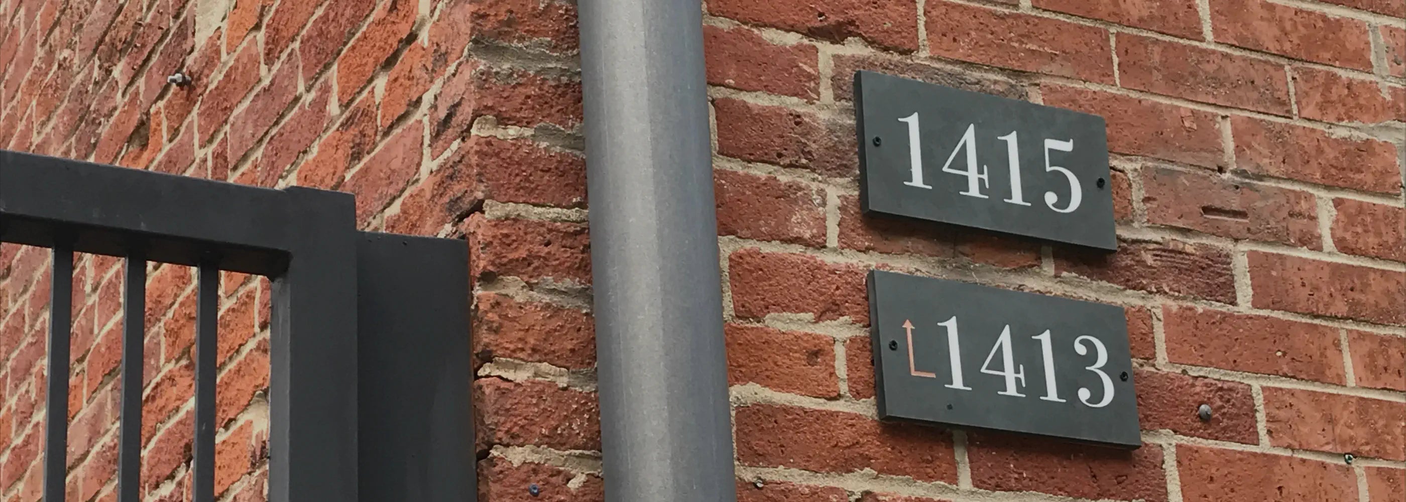 Engraved slate door numbers '1415' and '11413' on a brick wall.