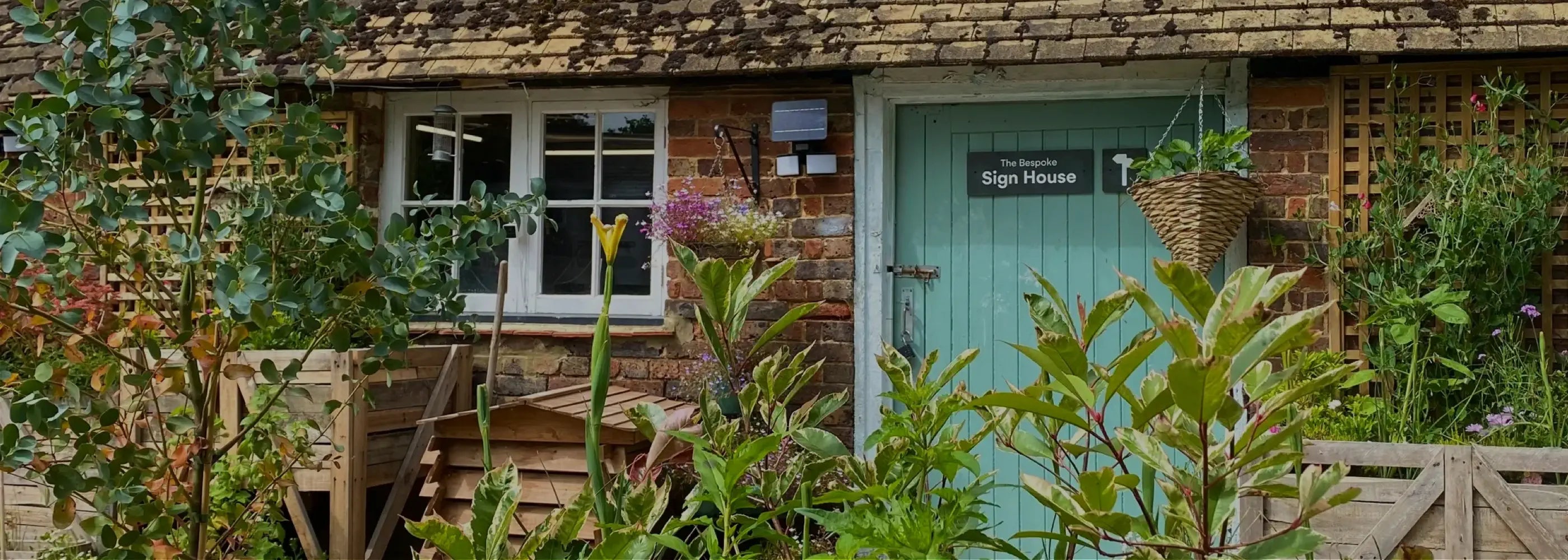Green door of a quaint workshop with plants and garden furniture around