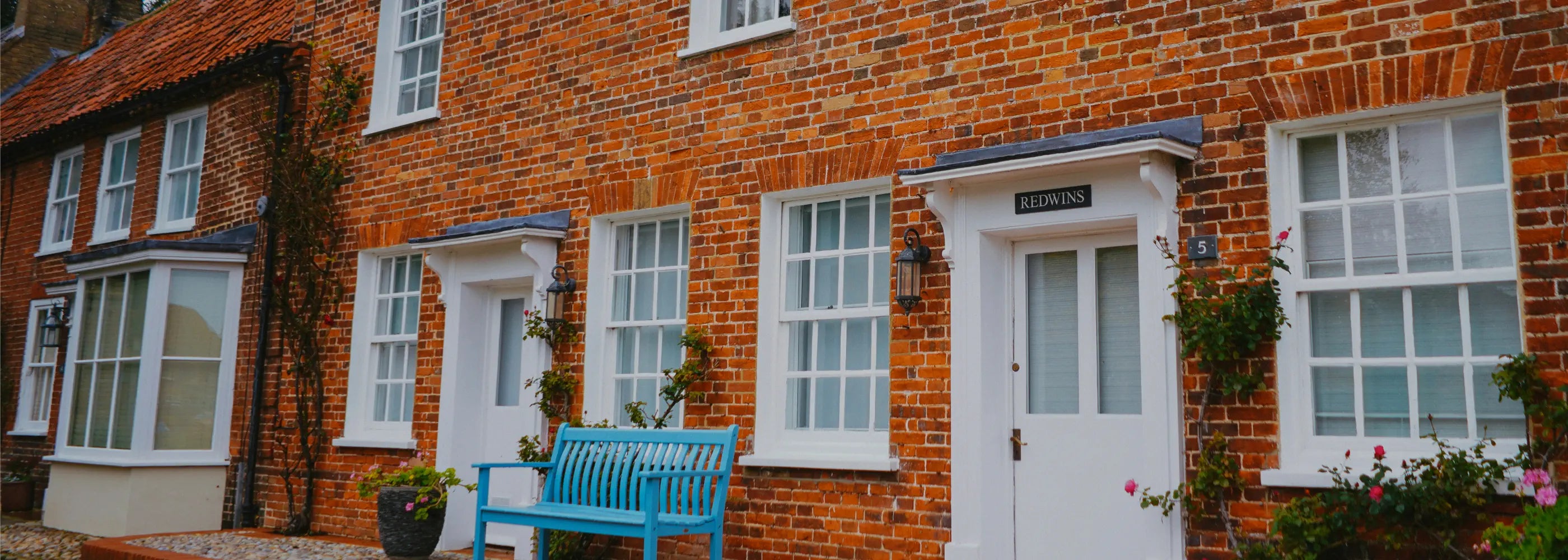 Brick building with white doors and windows, featuring a blue bench.