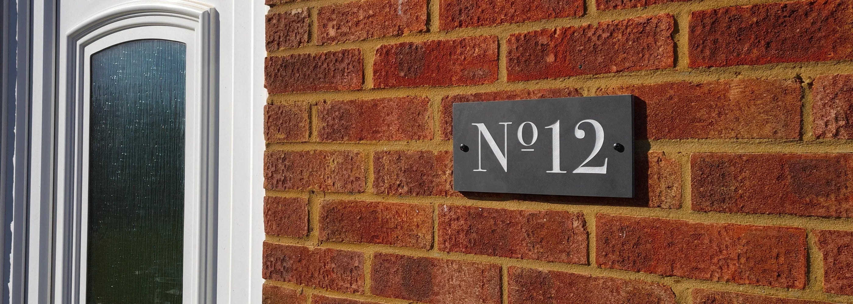 House number 'No. 12' on a brick wall next to a door with a glass panel.