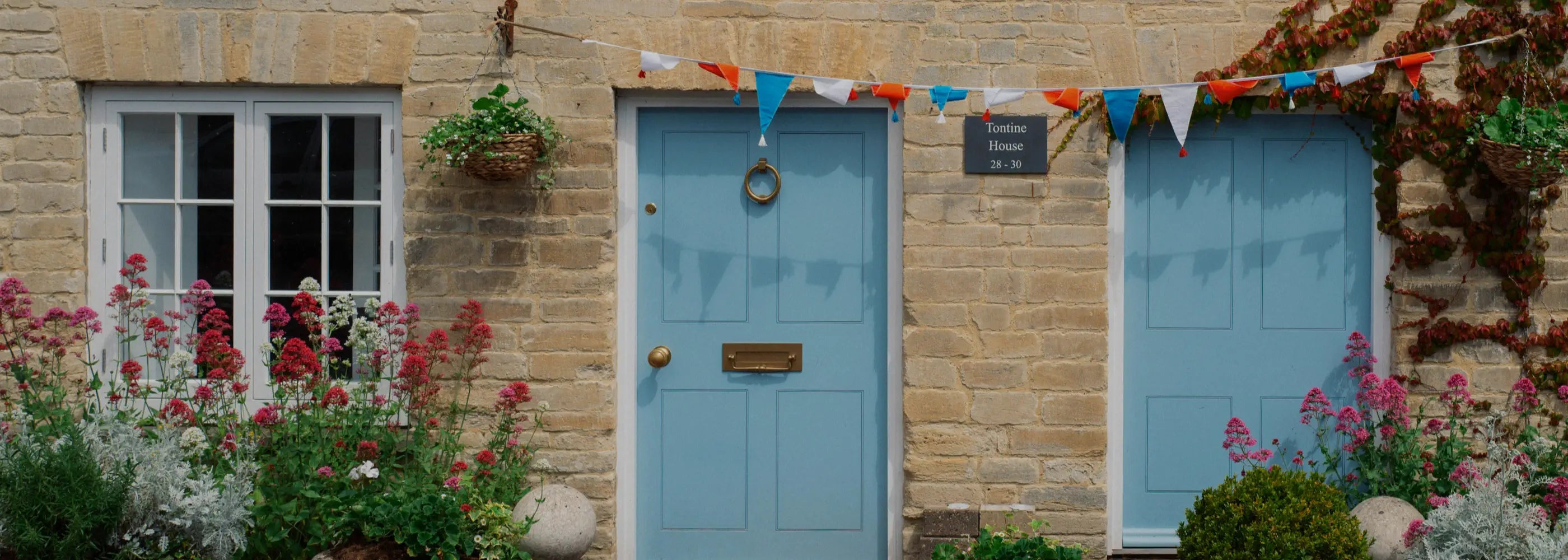 Blue door of a house with flowers and flags on a brick wall