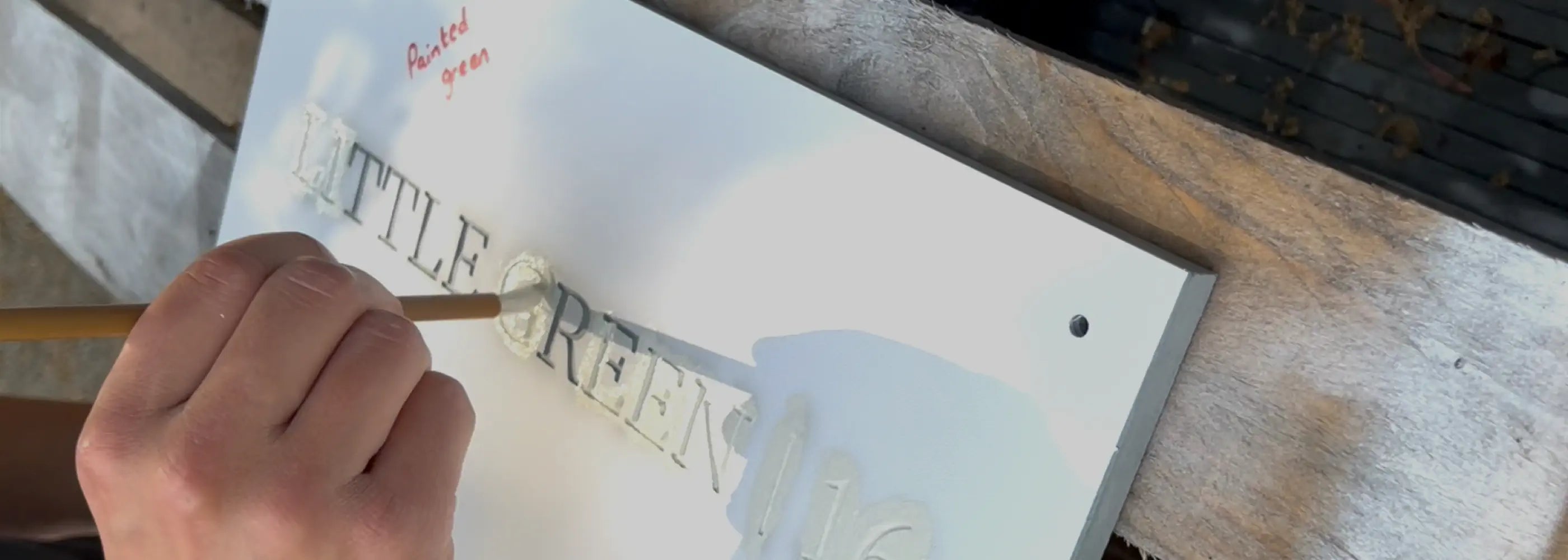 Hand-painting a slate house sign with a brush using green paint