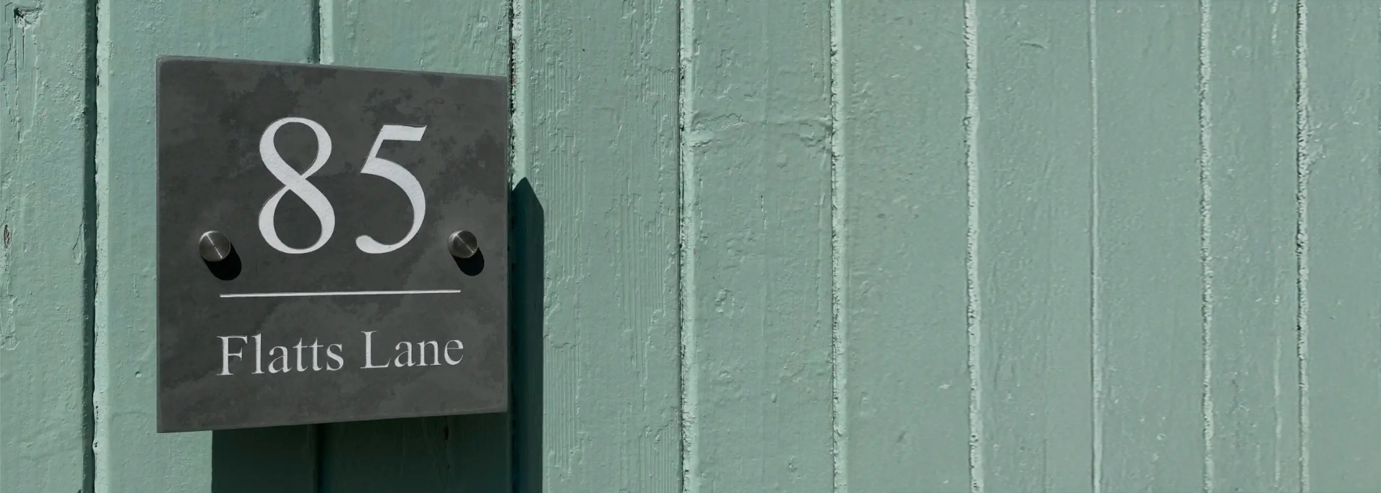 House number sign on a green door with silver screw caps