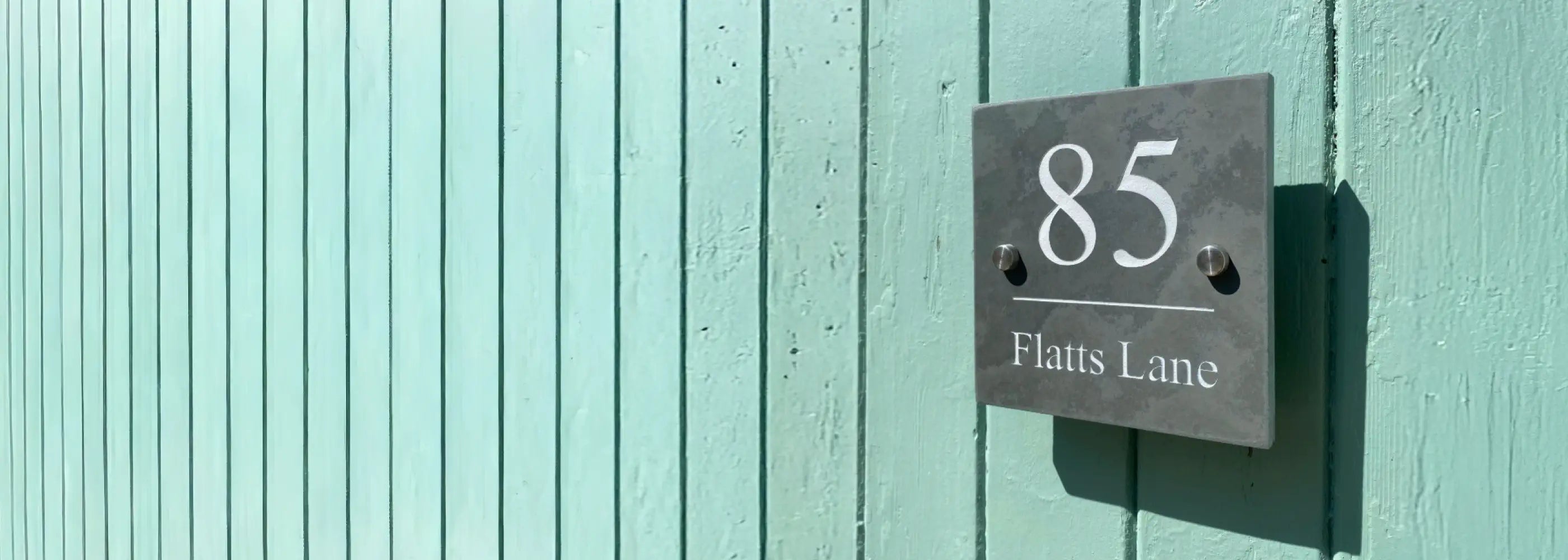 House number sign on a green door with silver screw caps