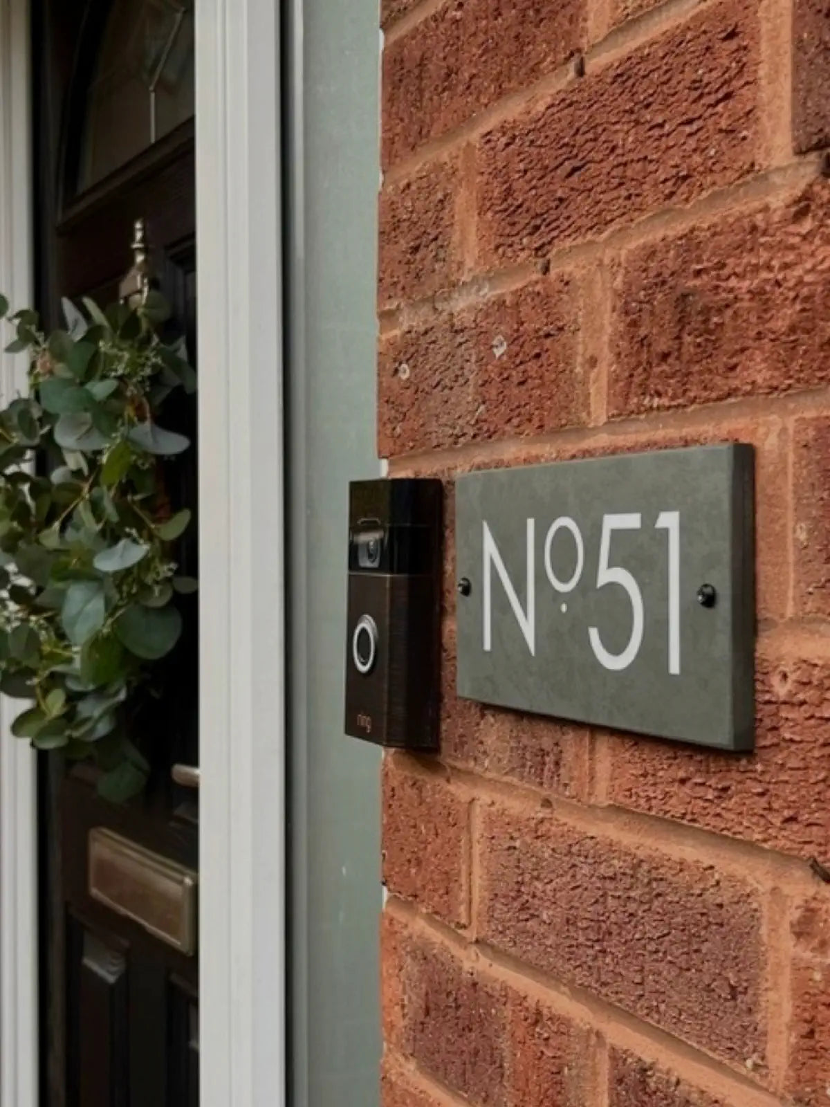 House number 'No. 51' next to a door bell on a brick wall next to a black door