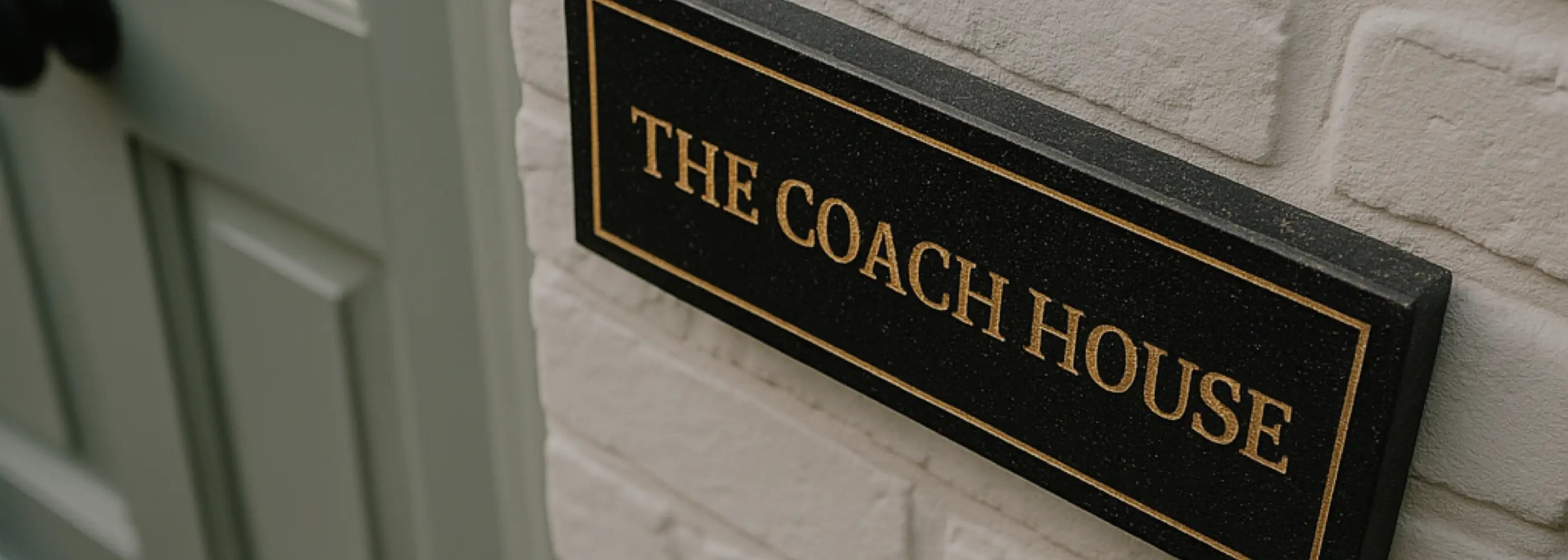 Black granite house sign with 'The Coach House' on a white brick wall
