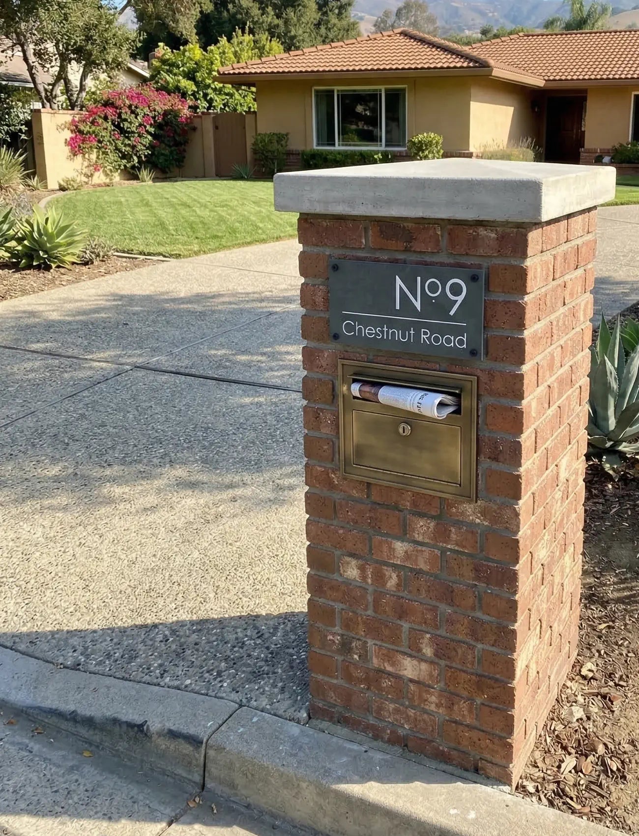 Brick mailbox with gold mail slot and address sign in front of a house