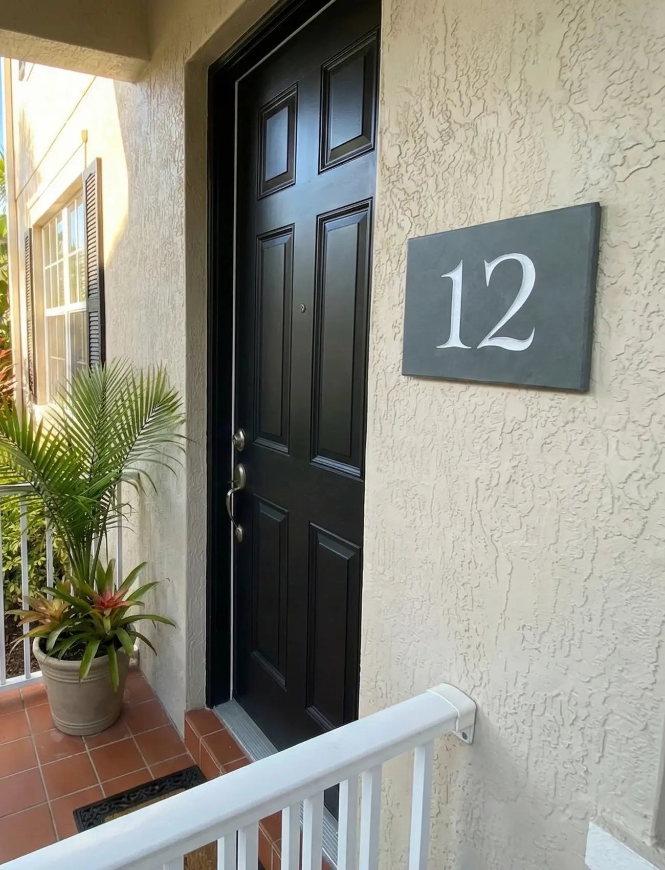 House exterior with a black door and slate house number 12 sign.