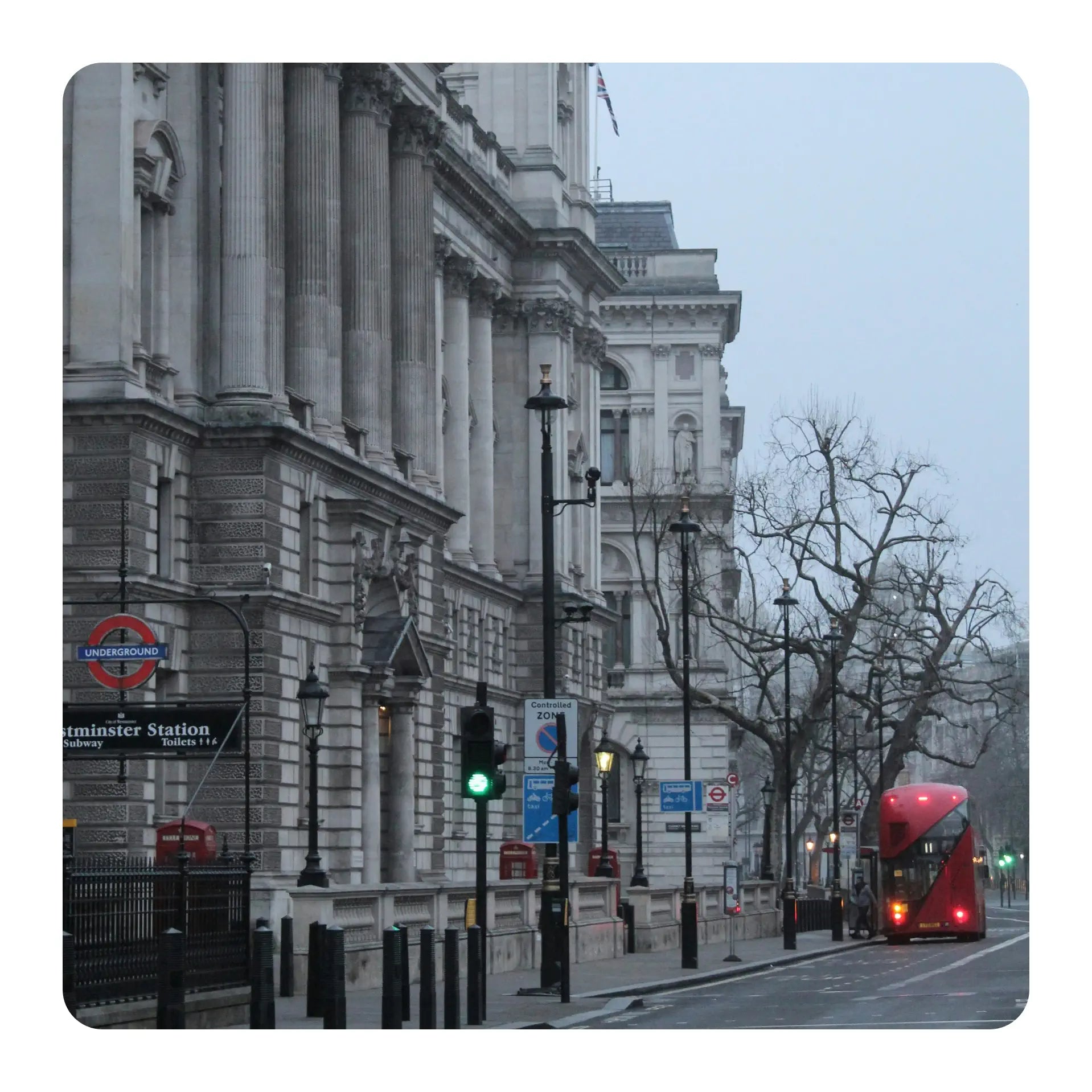City street with a double-decker bus in London, featuring a large building and traffic lights.