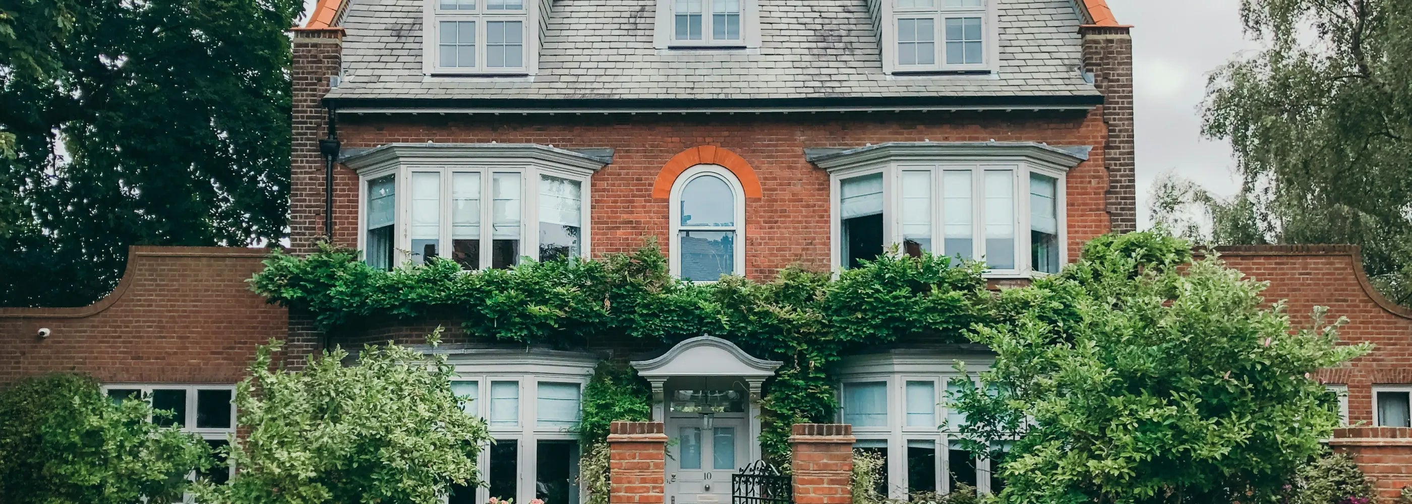 Large brick house with greenery on the roof and windows, surrounded by trees.