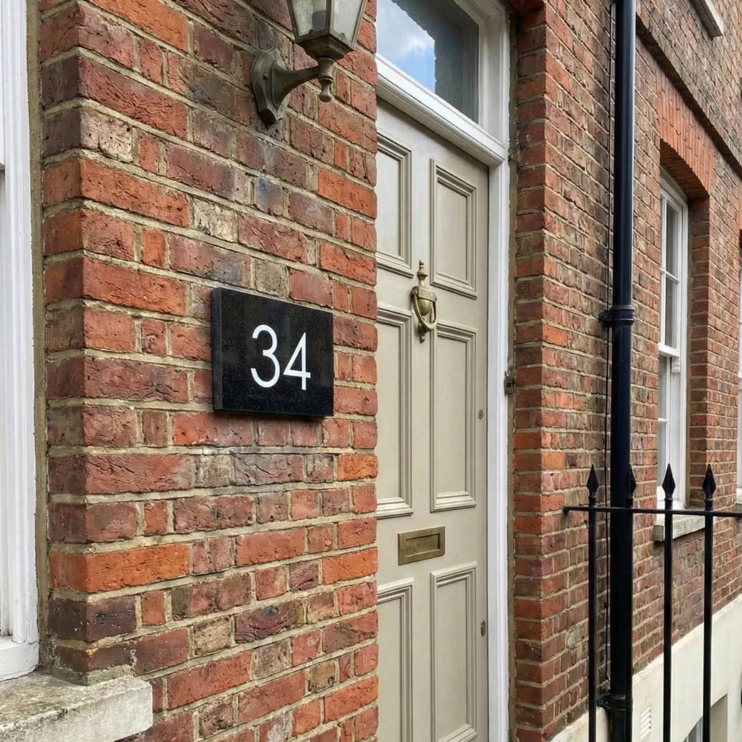 A black granite door number sign with the number 34 engraved in white. The sign is displayed on a white wall.