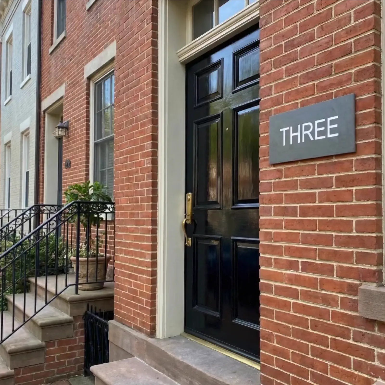 Brick building with a black door and 'THREE' address plaque made of slate.