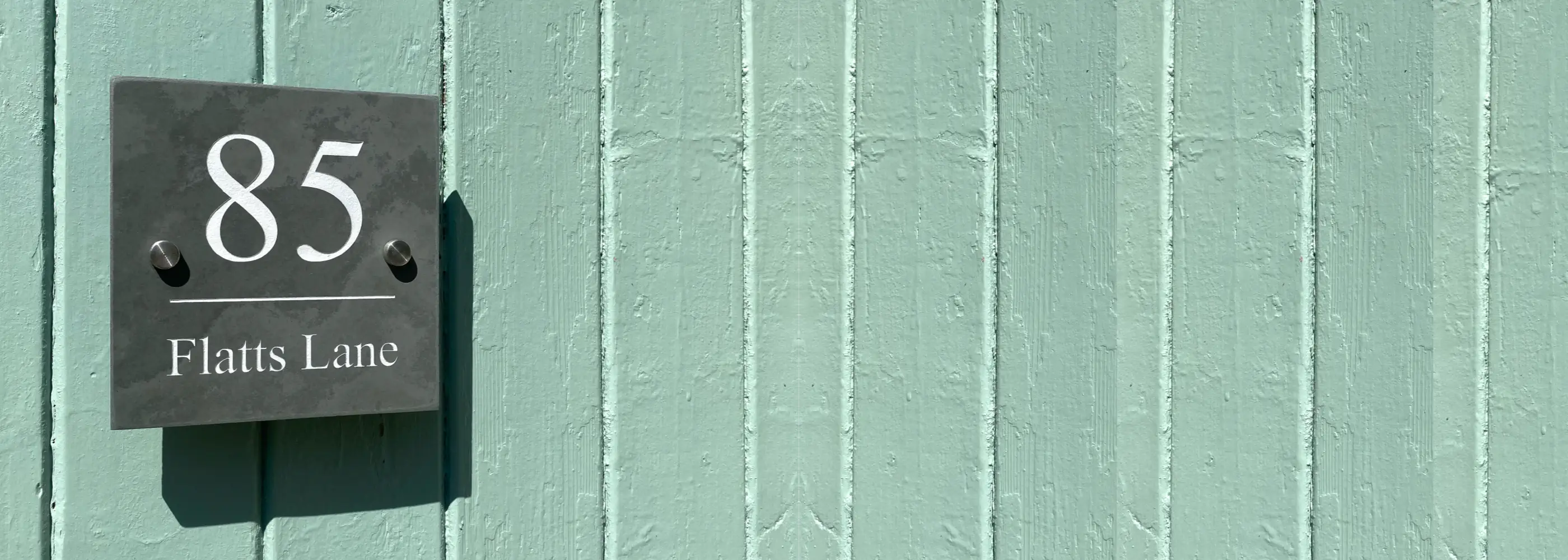 House number sign with '85 Flatts Lane' on a teal wall
