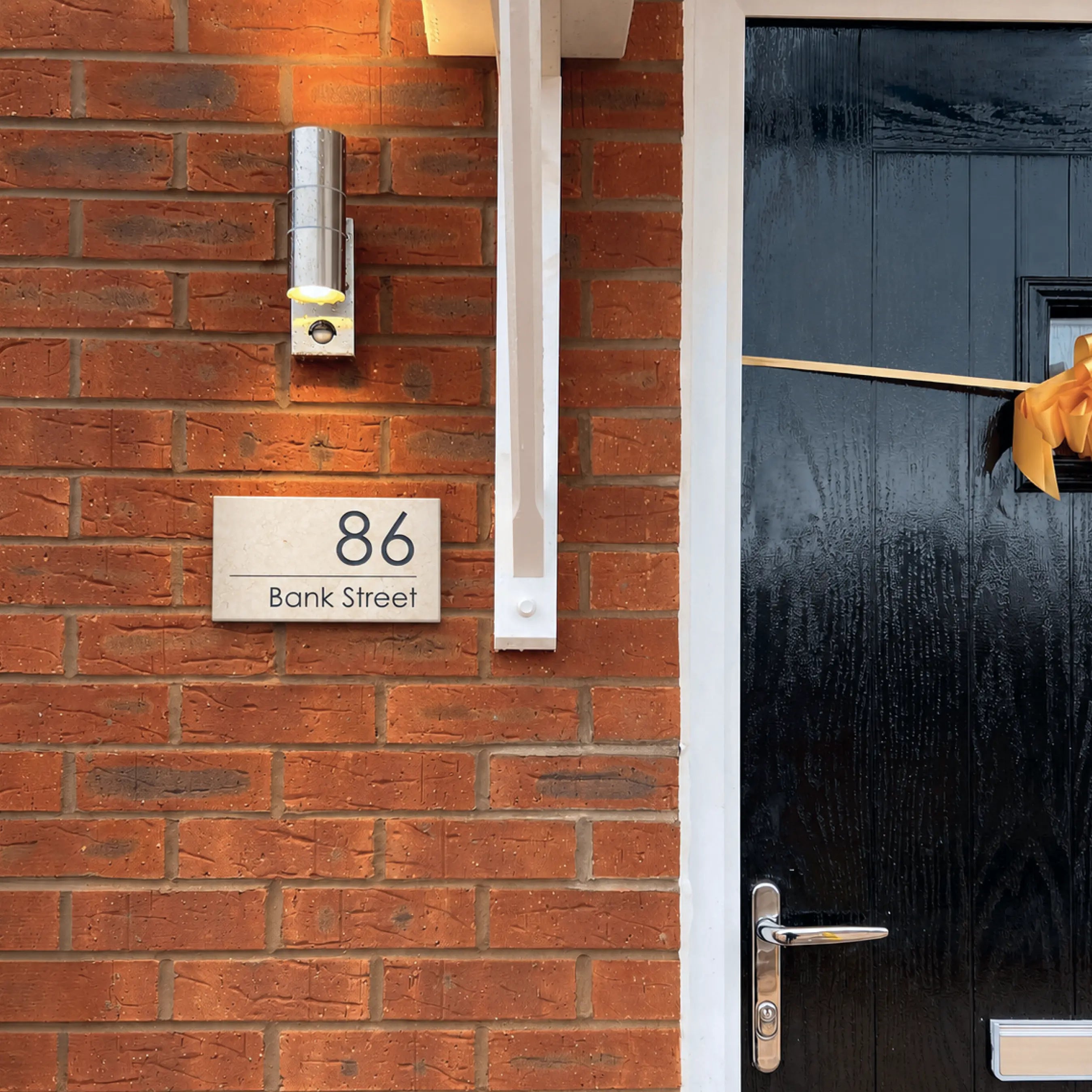 Blue door with house number 72 on a brick wall, garden visible in the background