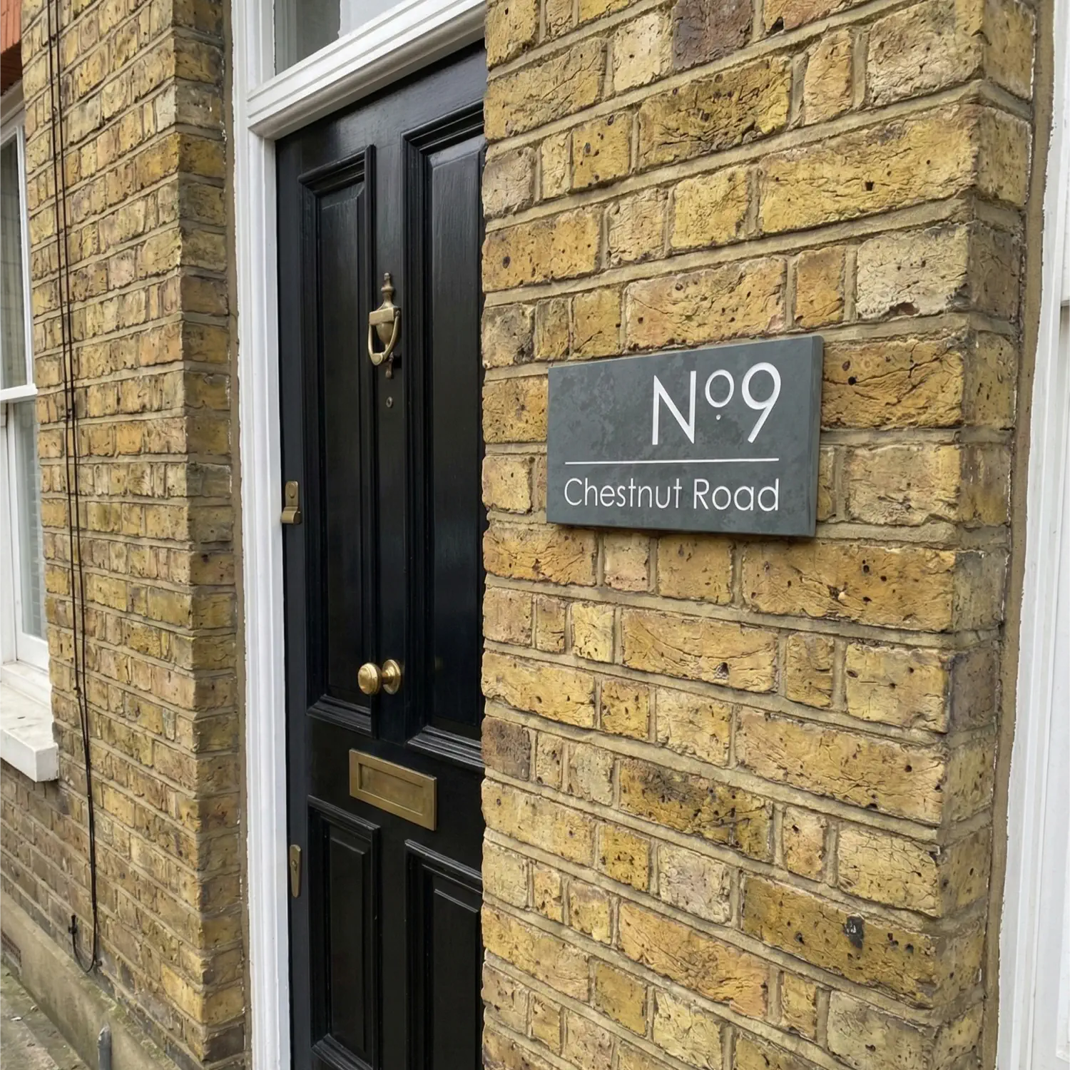 House number sign '9 Chestnut Road' on a brick wall next to a door.