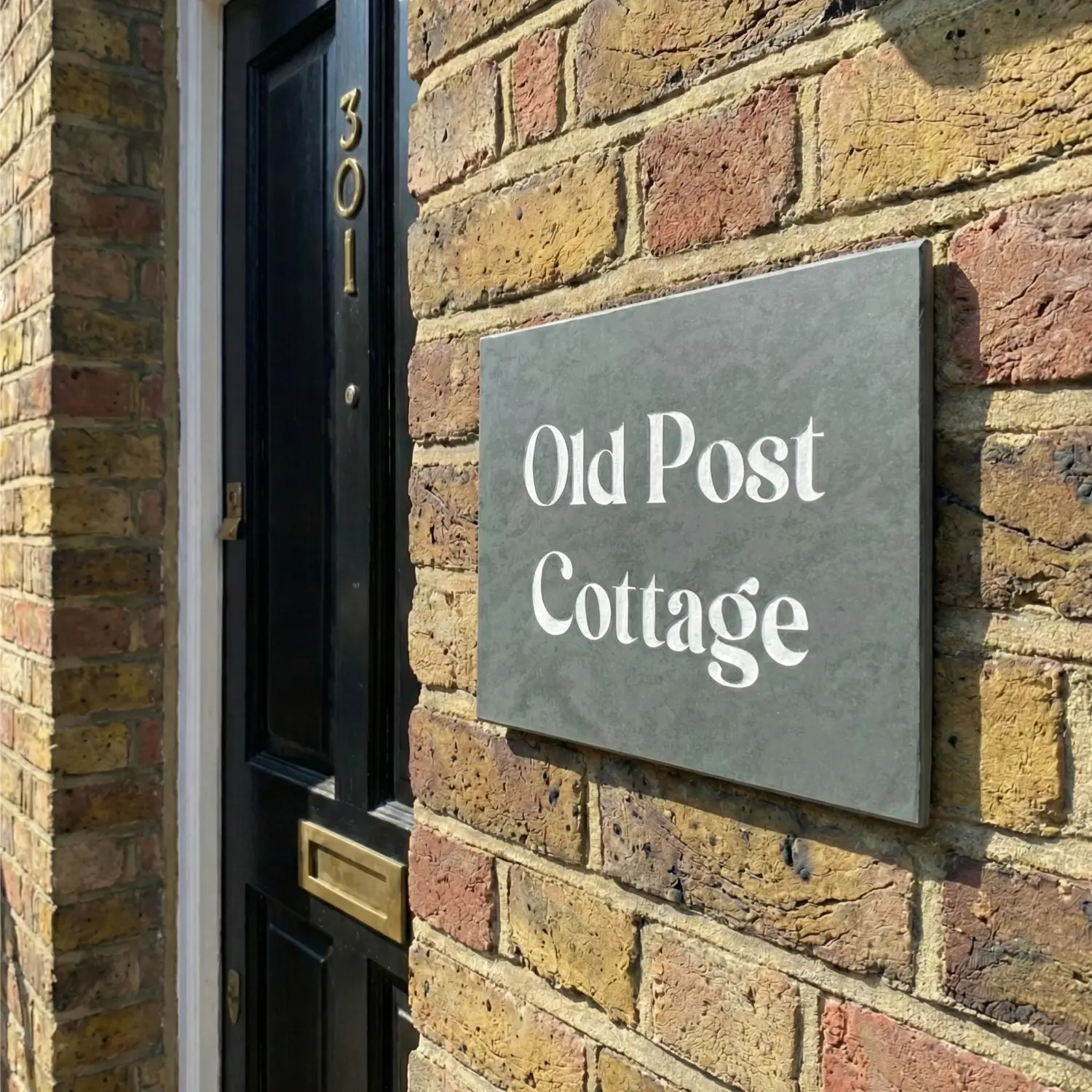 a grey slate house sign on a red brick wall reading The Weald.