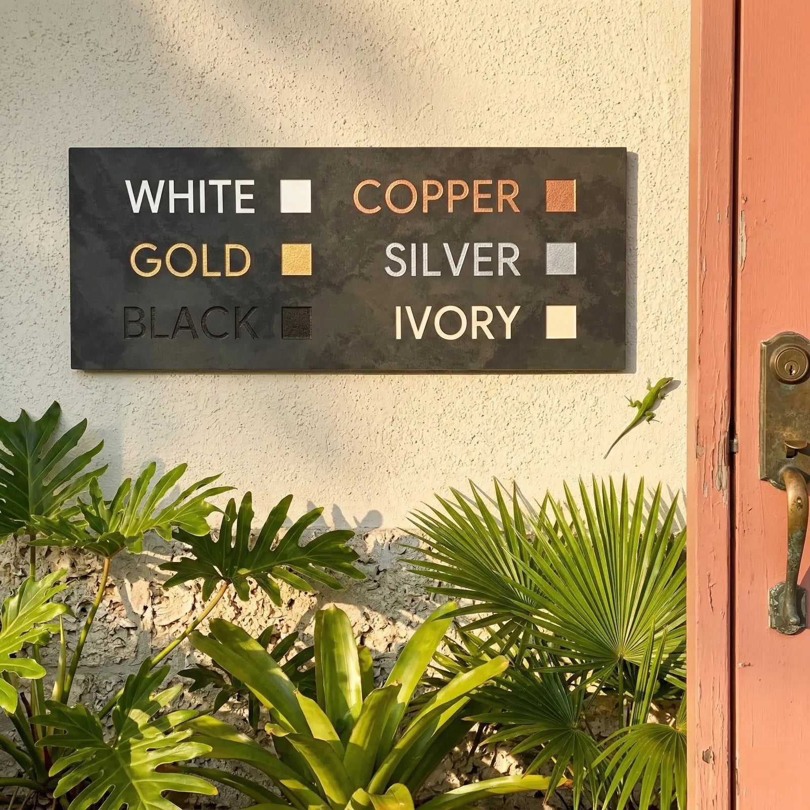 Color swatch panel with text labels on a textured wall with plants and a door handle.