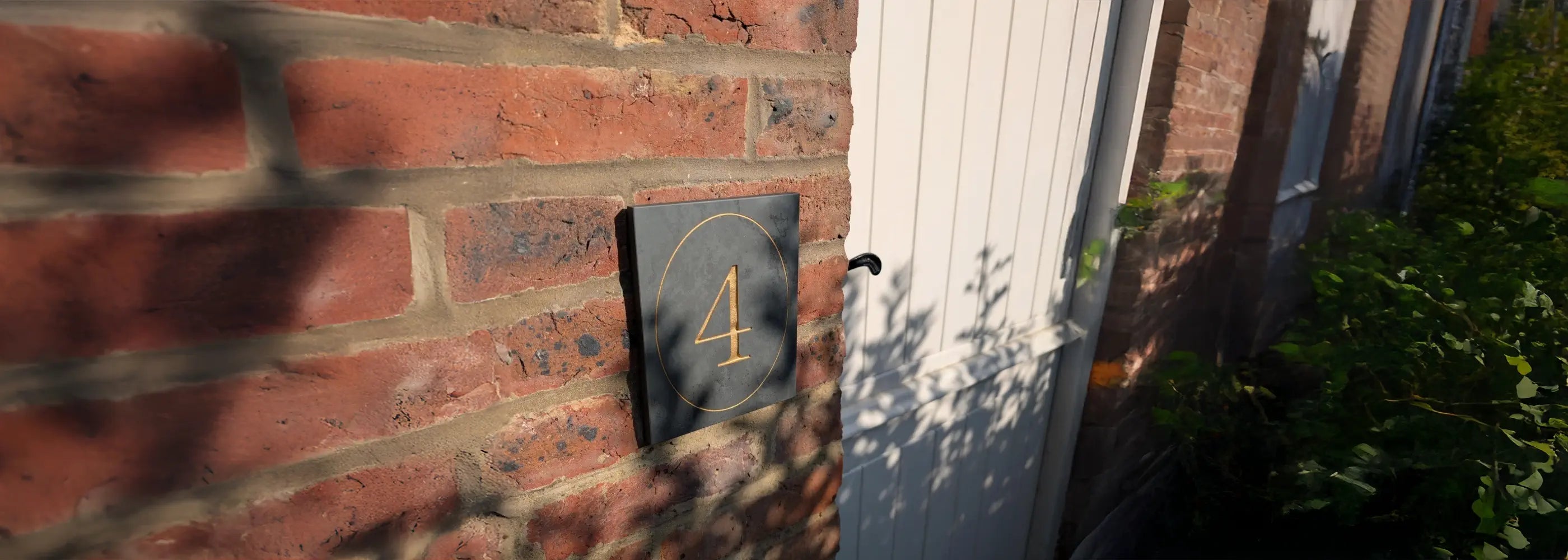 House number '4' stylised in oval on a black plaque attached to a brick wall.
