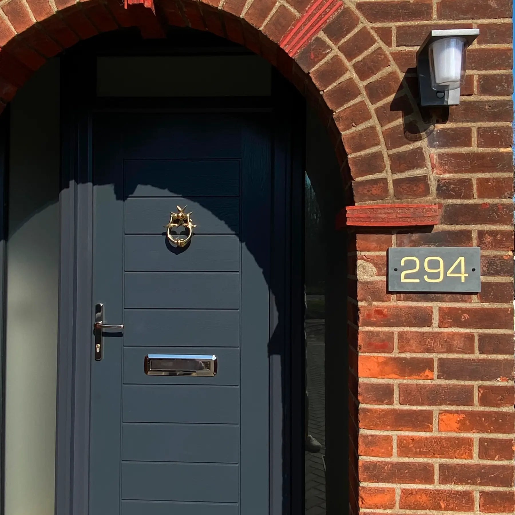 Blue door with gold knocker and number 294 on a brick wall