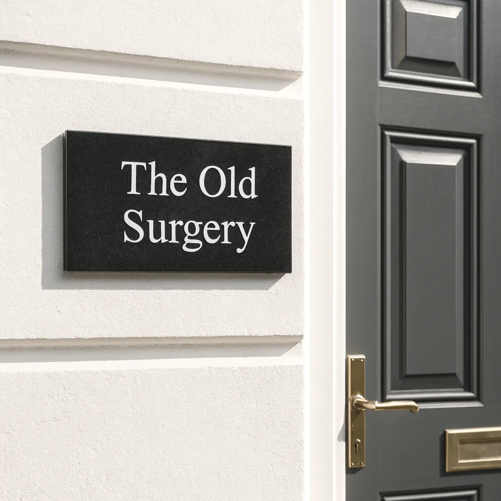 Black granite sign with 'The Old Surgery' on a brick wall next to a door.