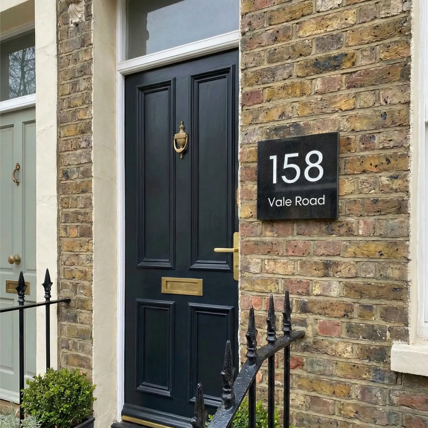 a black granite house sign with 158 vale road engraved and painted white. the sign is balancing on cut up logs