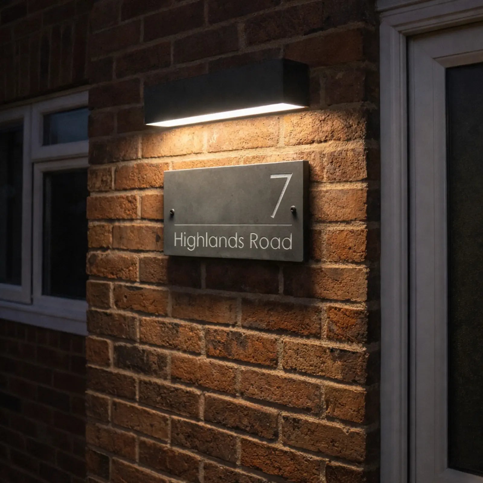 Modern house number sign on a brick wall with a light fixture above.