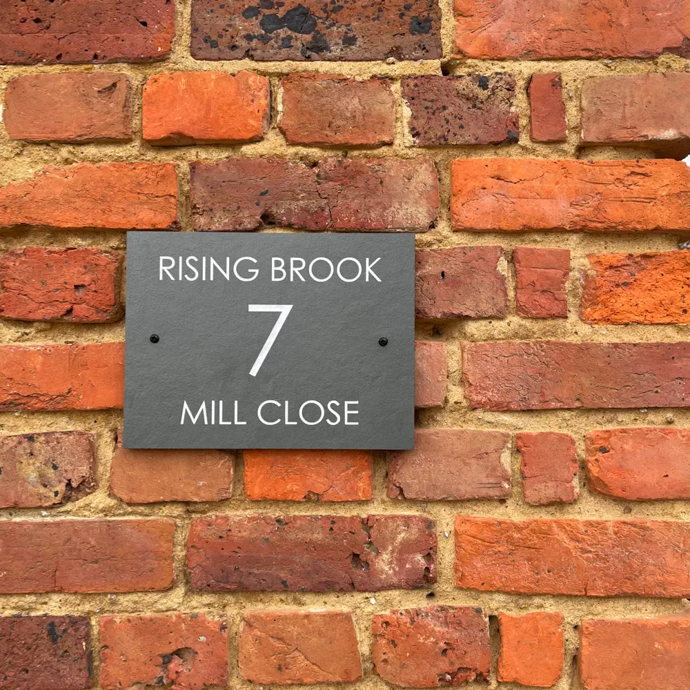Slate address sign on a brick wall with 'Rising Brook 7 Mill Close' text.