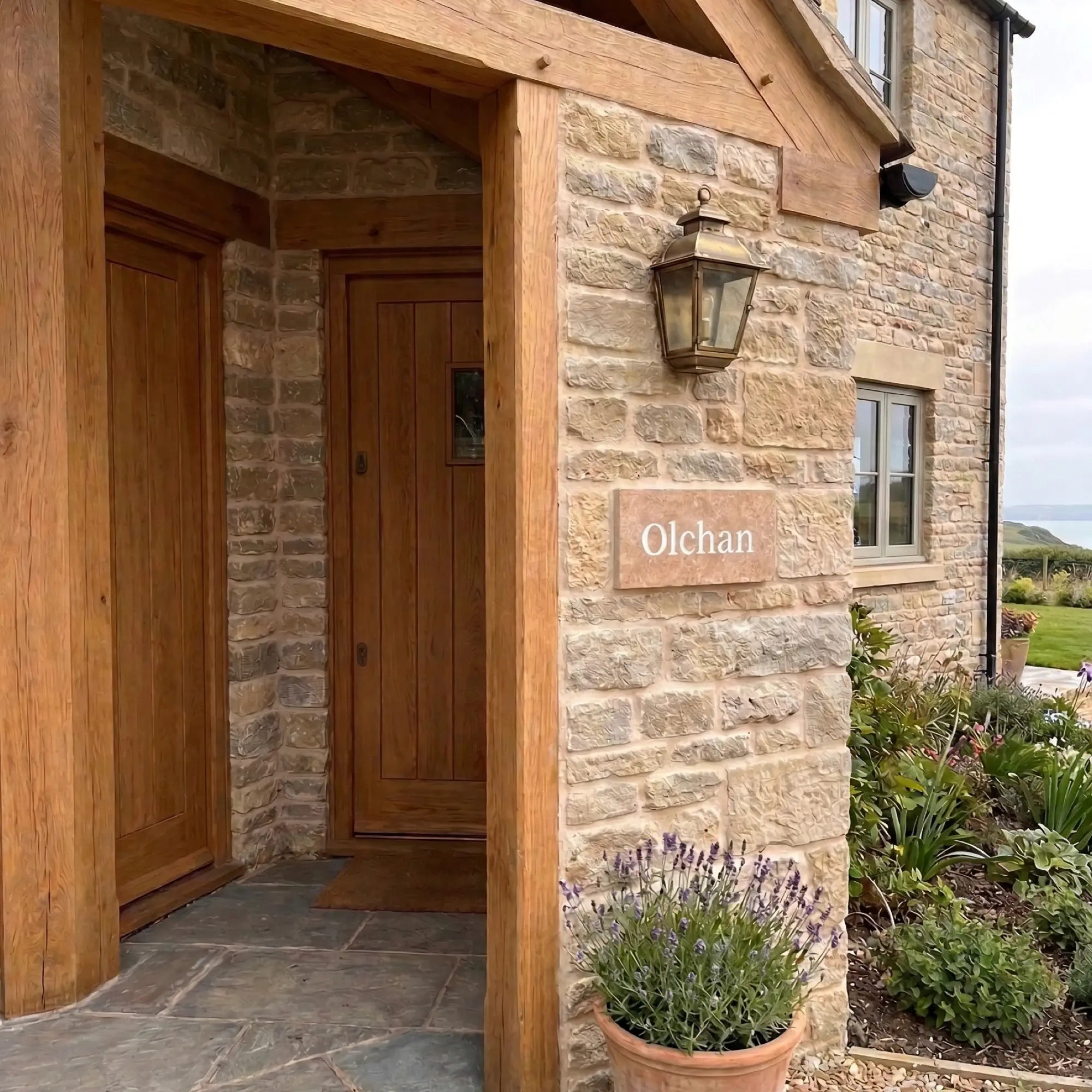 Stone building with wooden doors and a nameplate reading 'Olchan', surrounded by plants and a garden.