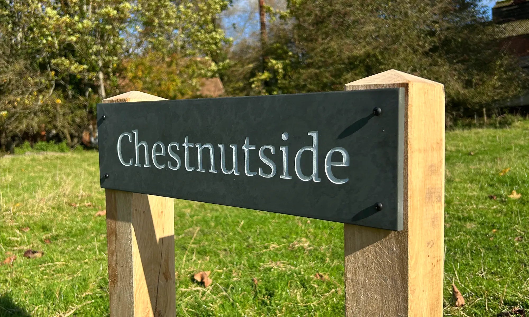 Slate house sign reading “Chestnutside,” mounted on two oak posts with pyramid tops, set against a grassy outdoor background.