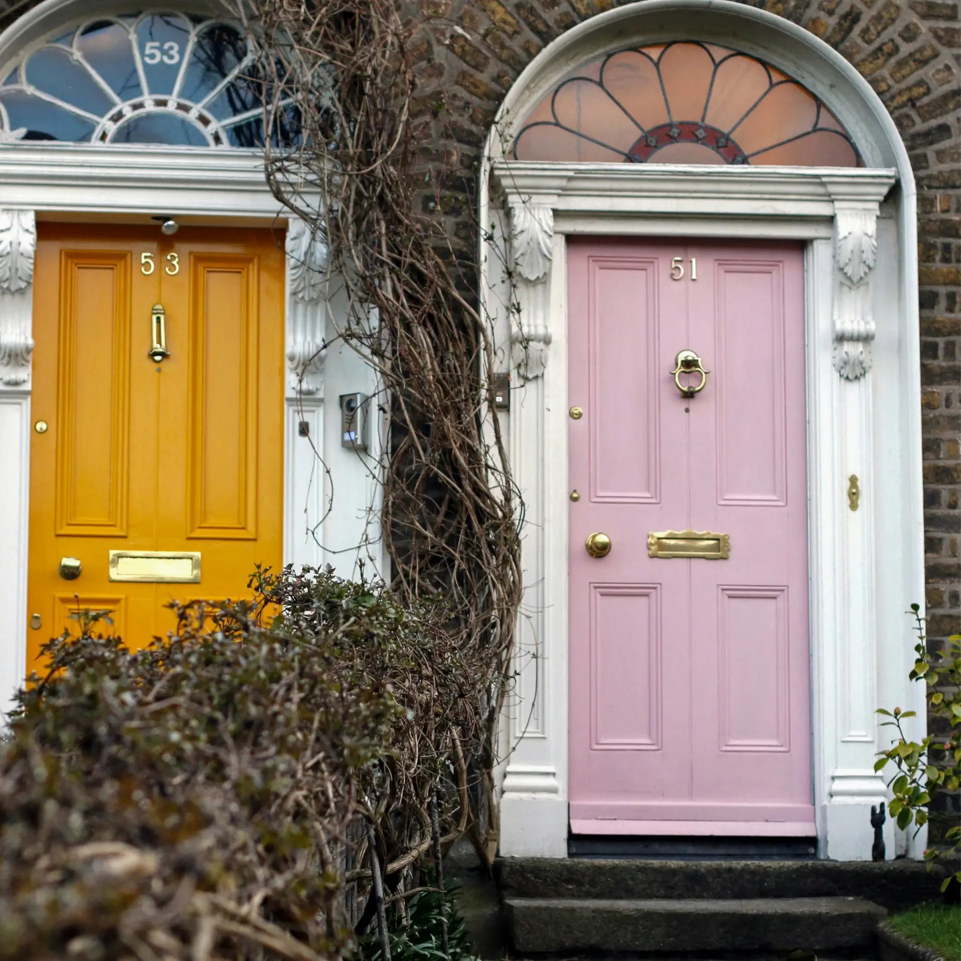 Two colourful front doors of a house, one yellow and one pink, with decorative elements.