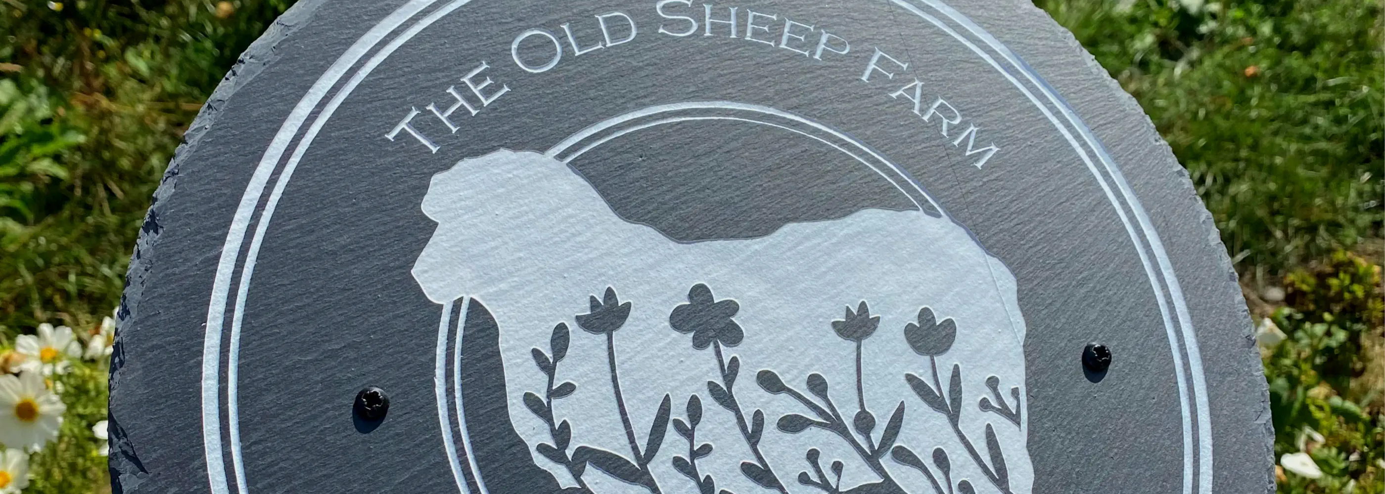 Round slate sign with sheep silhouette and 'The Old Sheep Farm' text on a grassy background