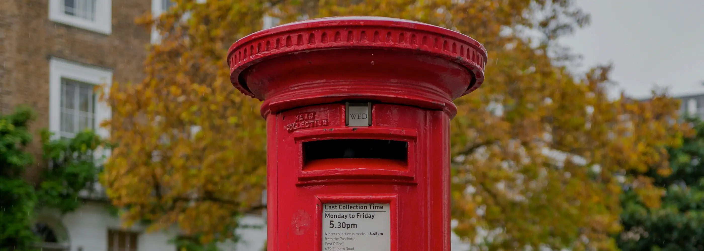 Red British postbox with autumn foliage in the background