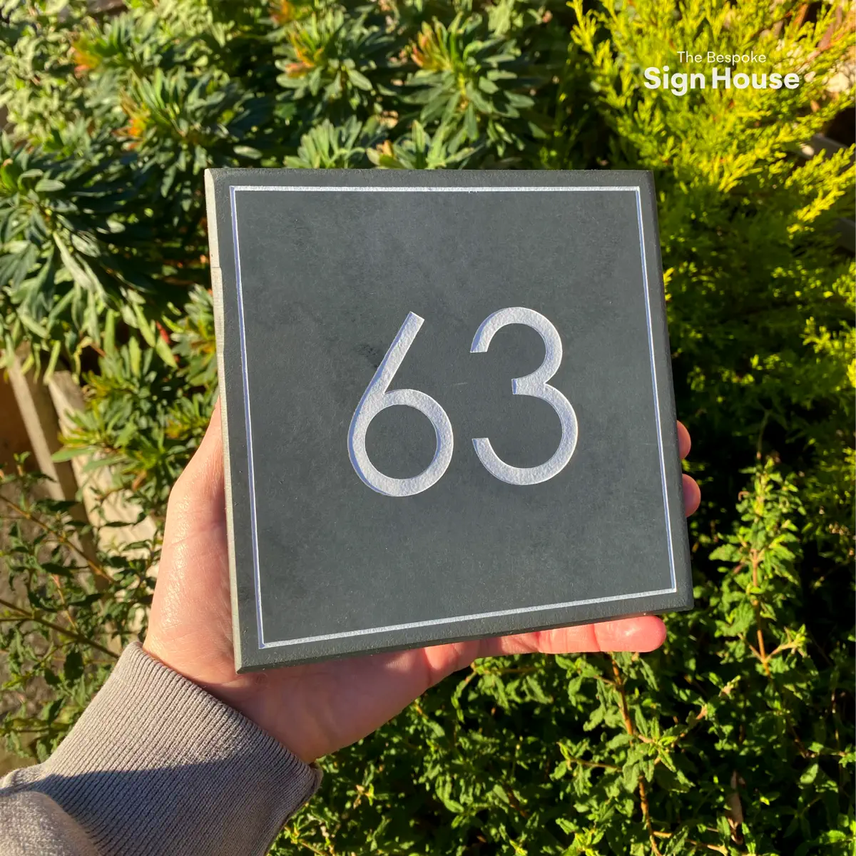 a slate sign with a number engraved and painted into the sign. The sign reads 63 in a modern font