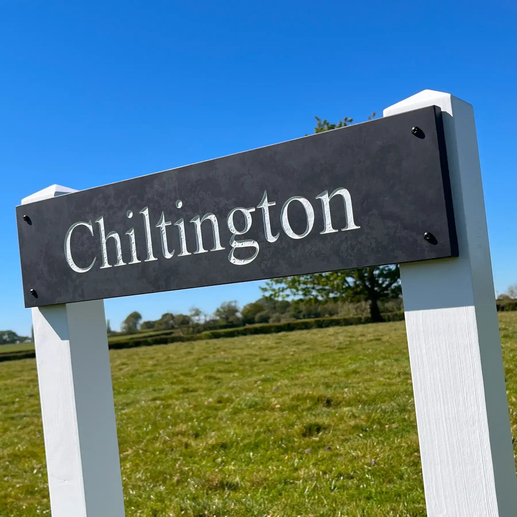 Signpost with 'Chiltington' text against a blue sky and green field background