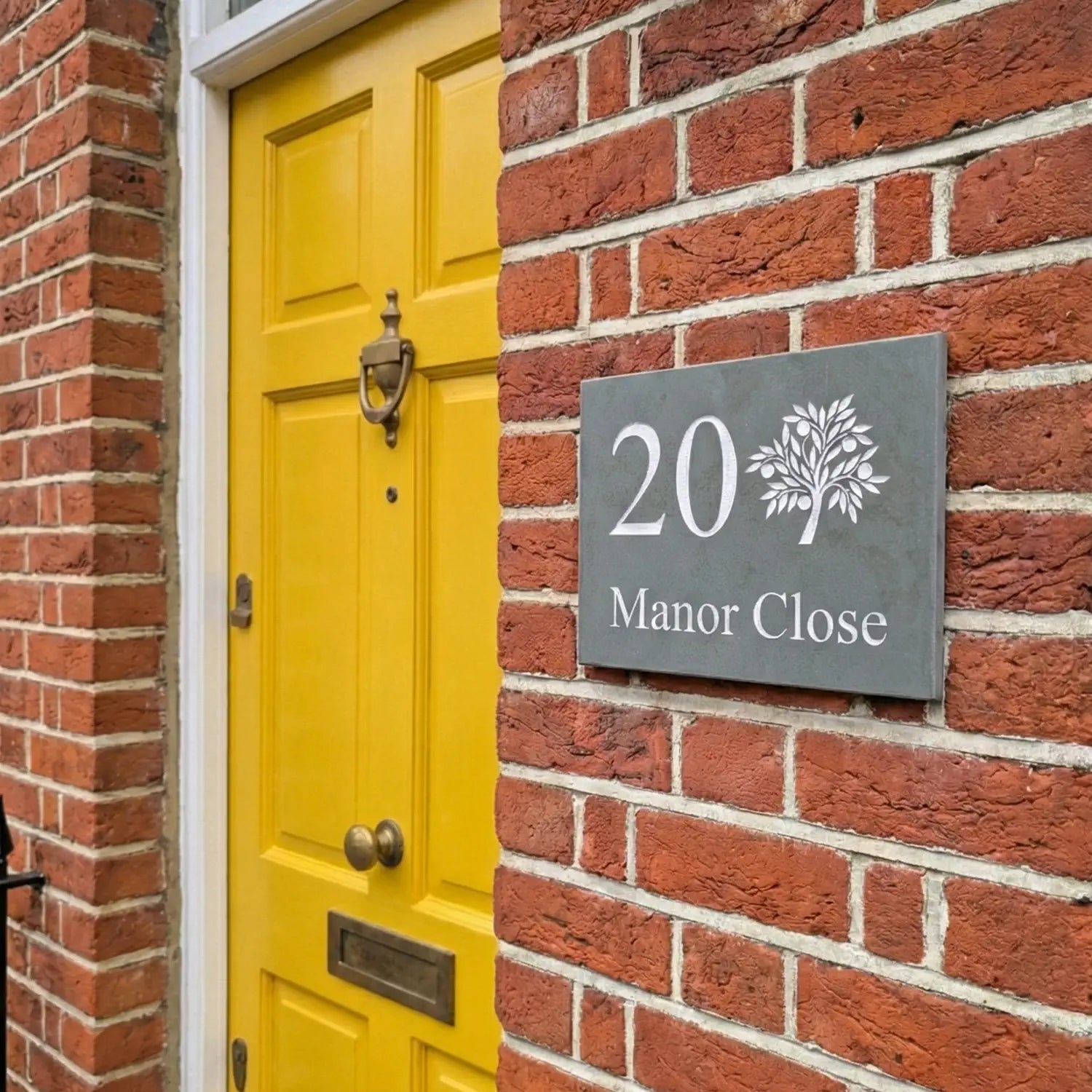 A preview of a slate house sign with a tree and house name, fixed onto a brick wall of a house.