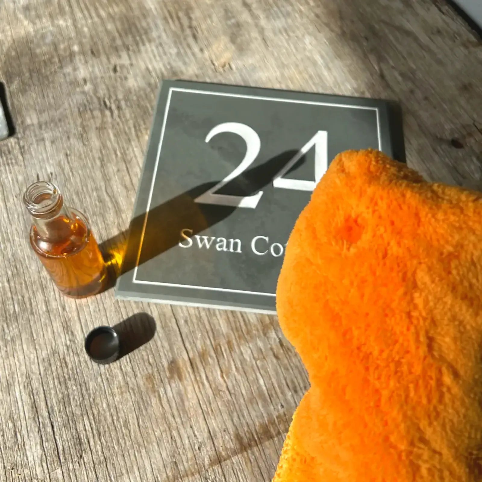 Orange bottle with black cap and orange towel on a light gray background