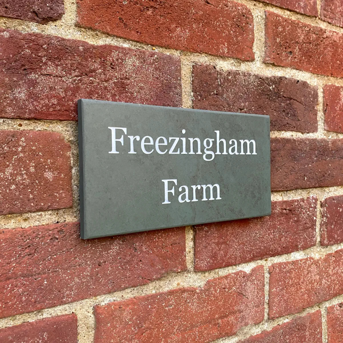 Slate house sign reading “Freezingham Farm” mounted on a red brick wall.