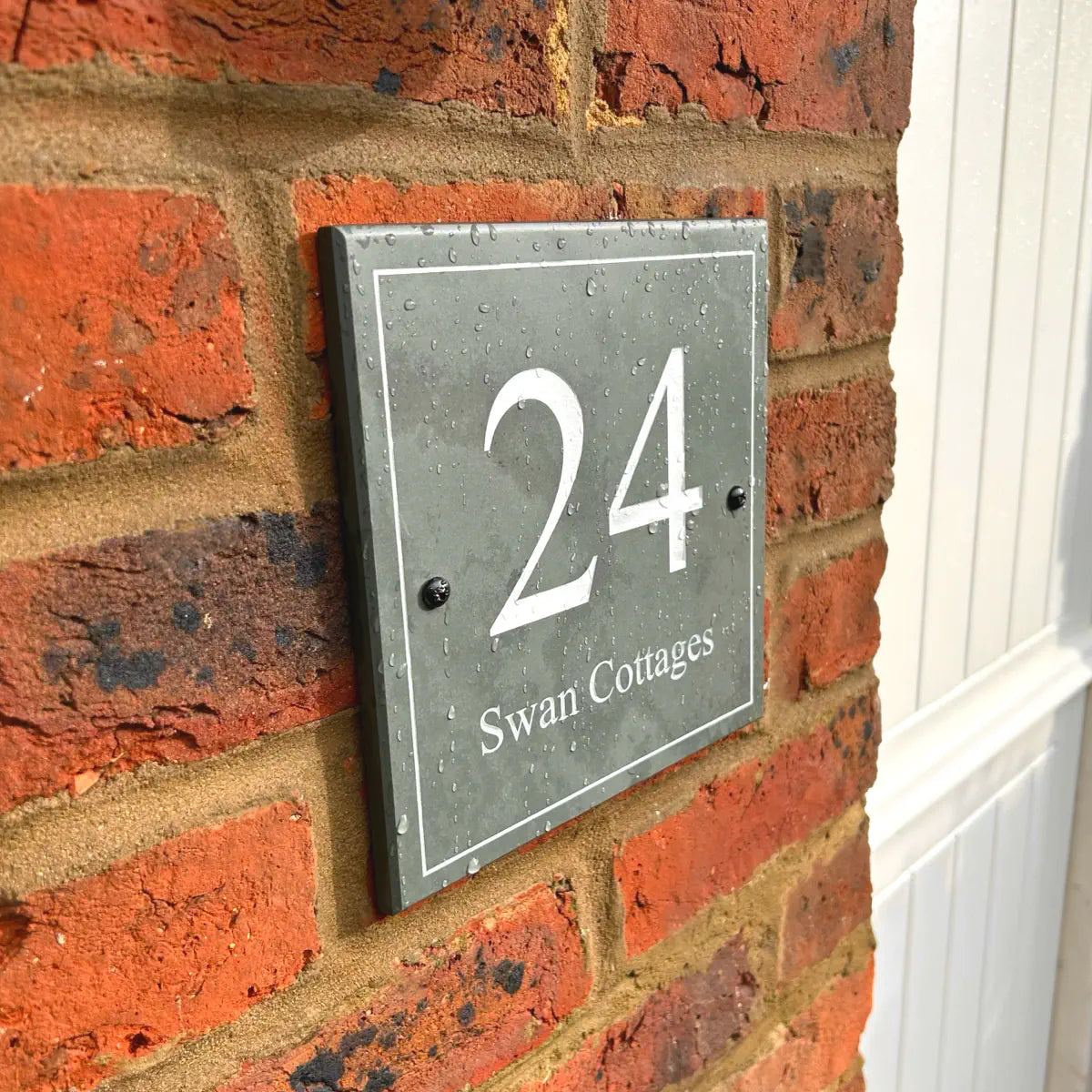 House number sign reading “24 Swan Cottages” mounted on a brick wall.