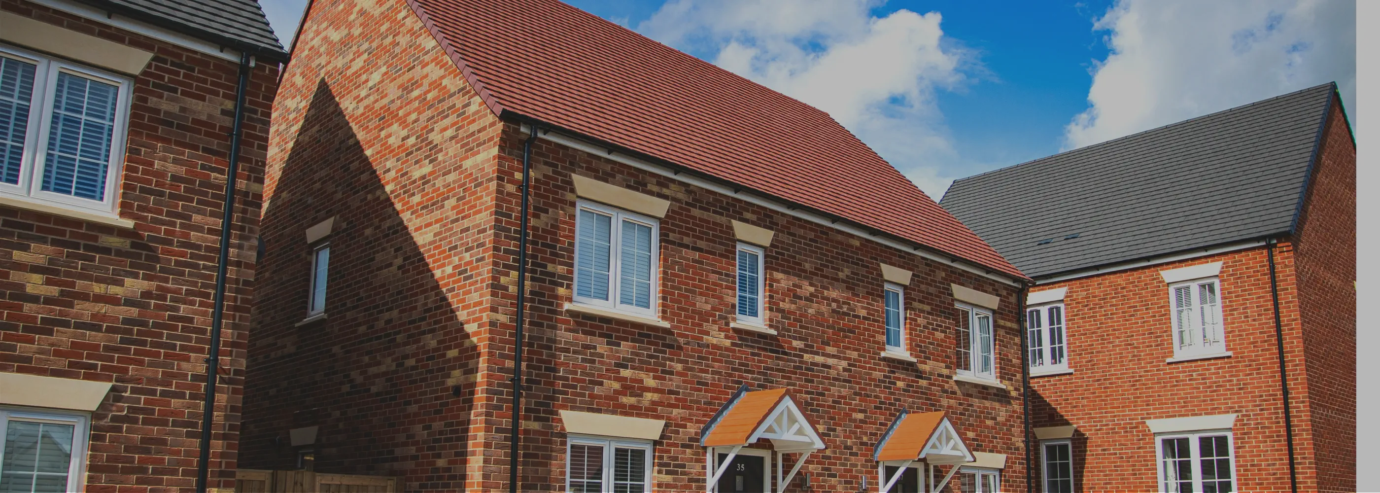 Row of brick houses with red roofs under a blue sky