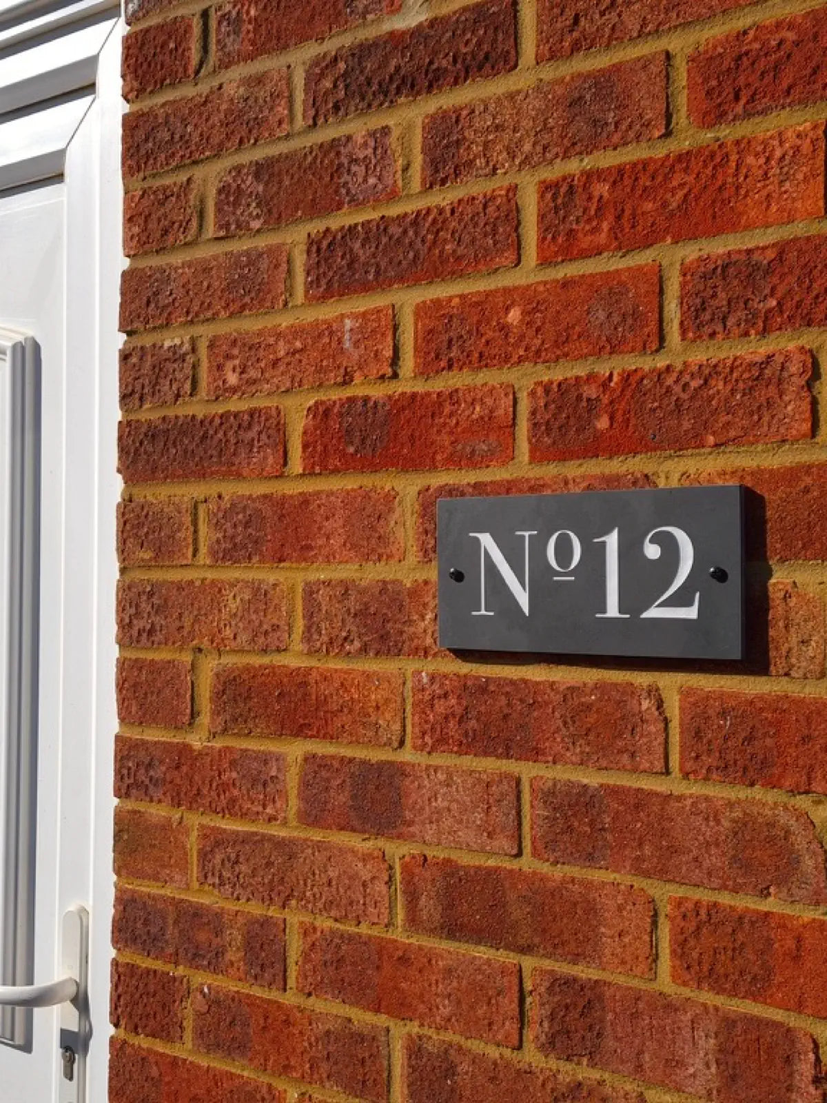 grey slate sign on brick wall reading number 12 in white