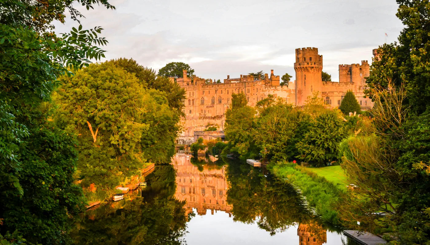 Warwick castle with reflection of trees and castle on lake