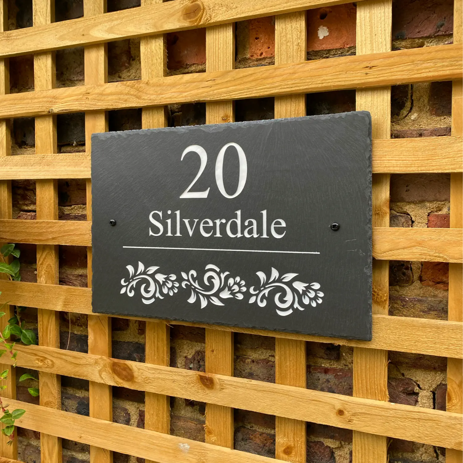 a welsh slate house sign with a house name, street number and floral design. Sign is positioned on a wooden trellis wall