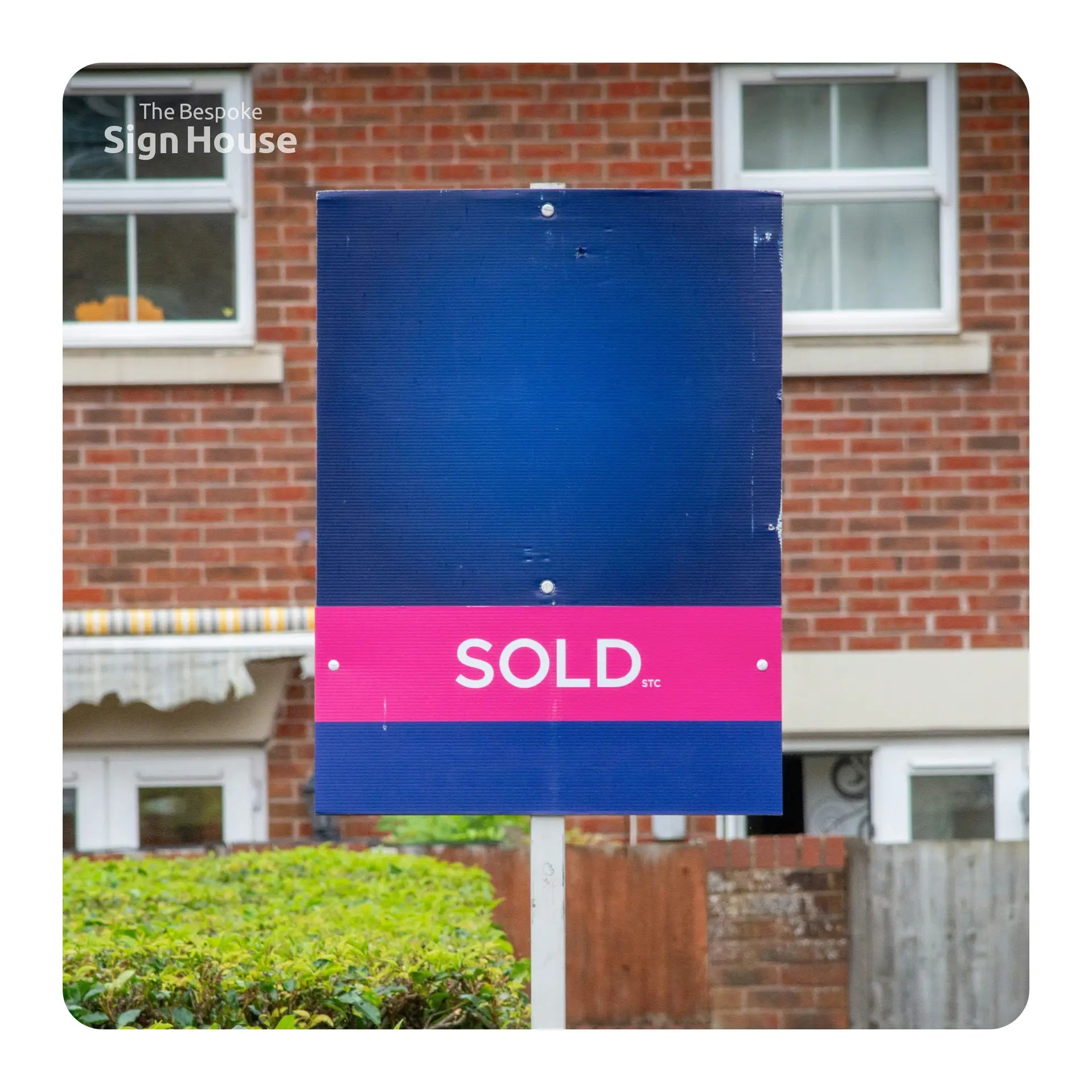 Blue and pink 'SOLD' sign in front of a brick house