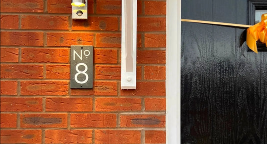 a slate house number sign on a red brick wall installed next to a black front door