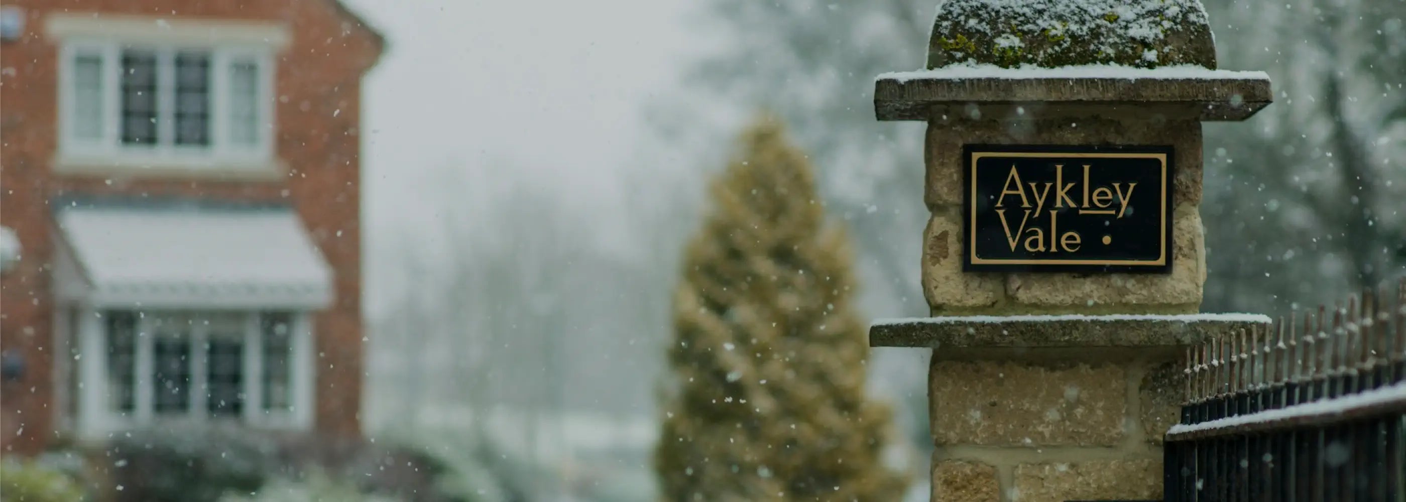 Granite house sign with 'Aykley Vale' sign in front of a house during snowfall
