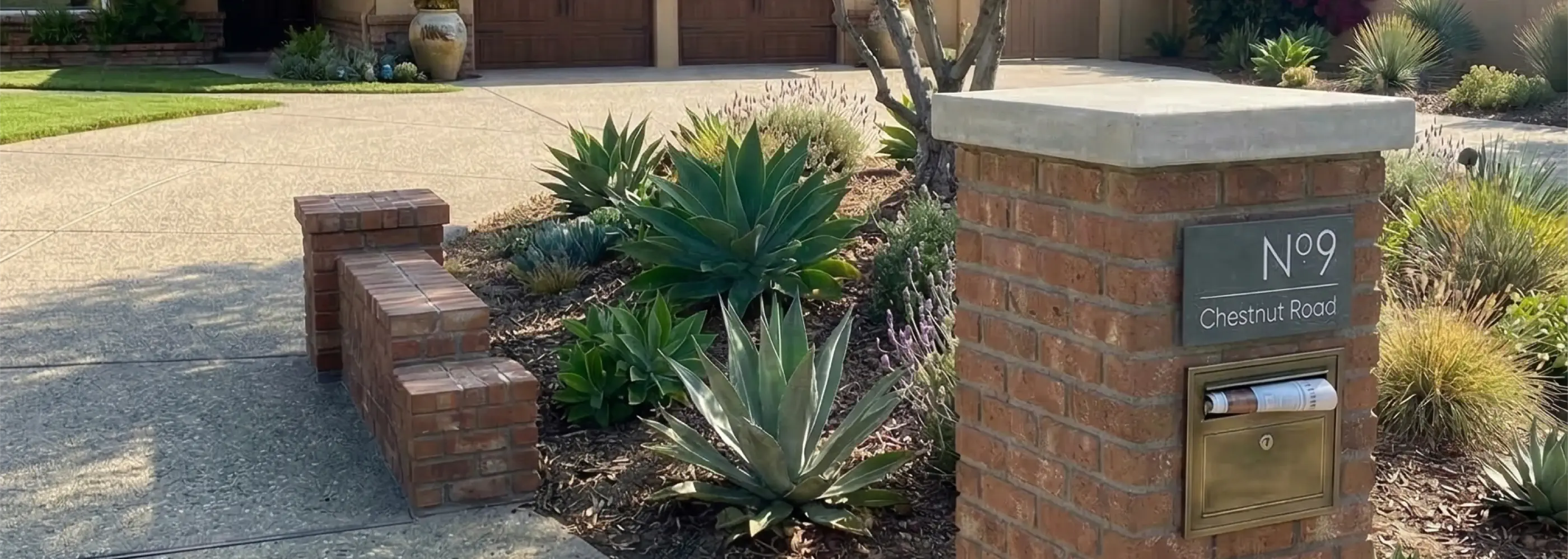 Brick mailbox with number 9 on a driveway with plants and steps.