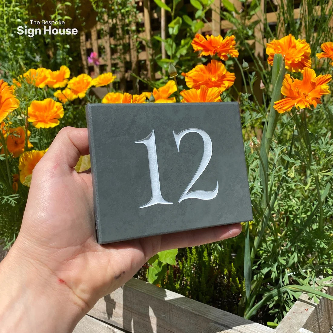 Slate house number sign deep engraved with the number 12 and painted white.