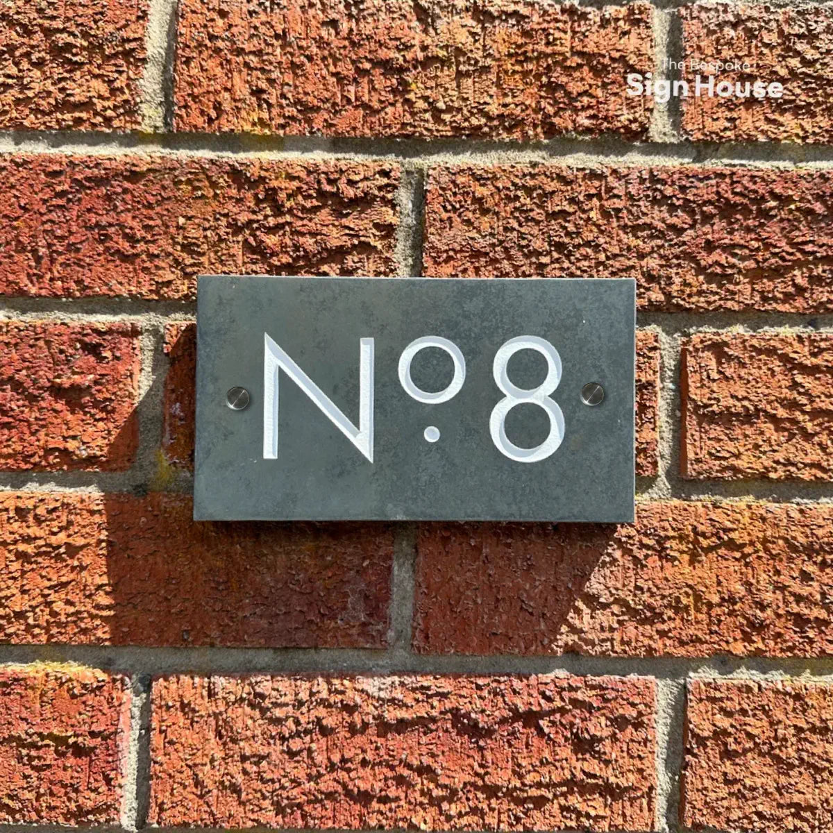 “Welsh slate house sign with ‘No. 8’ engraved in white, mounted on a red brick wall with two visible pre-drilled holes for mounting.”