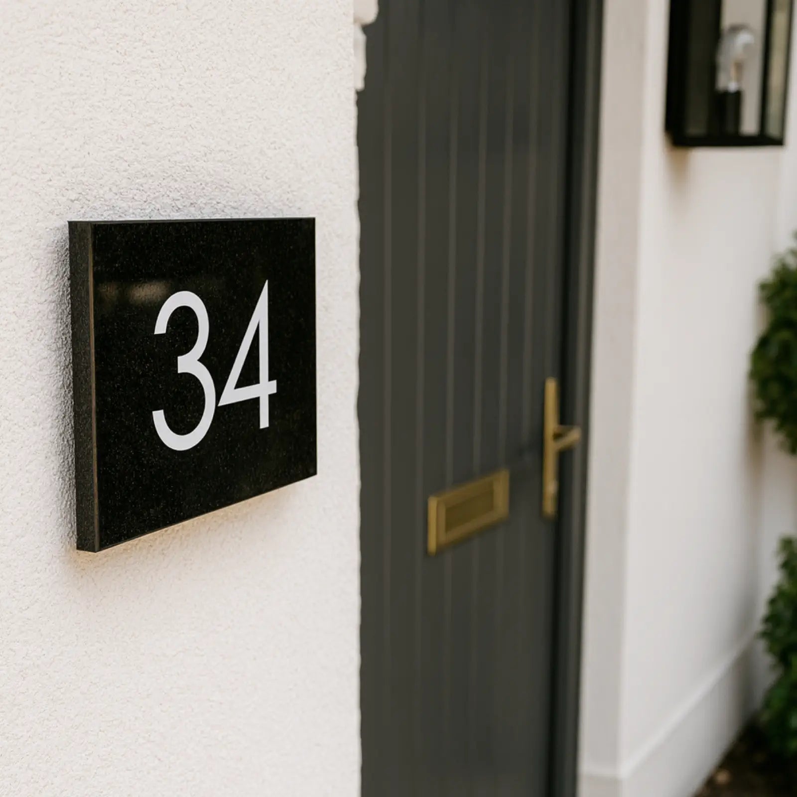 A black granite door number sign with the number 34 engraved in white. The sign is displayed on a white wall.