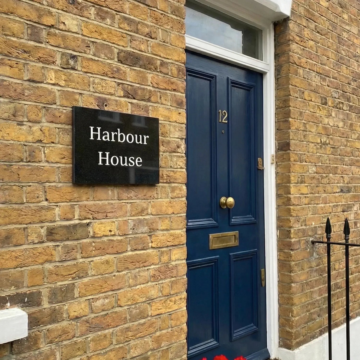 Black granite house sign reading 'Elmfield House' on a brick wall next to a blue door.